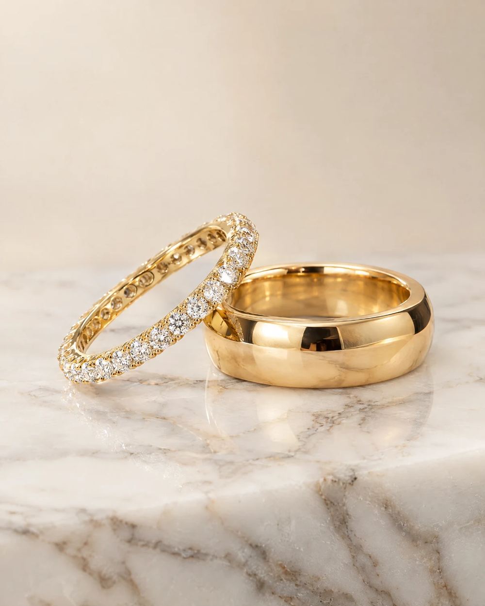 Yellow gold diamond eternity band beside a polished yellow gold men's wedding band on white marble